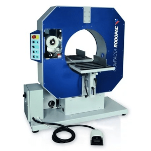 Industrial packaging machine (Robopac) with blue enclosure, circular load chamber, conveyor table, control panel, and foot pedal nearby.