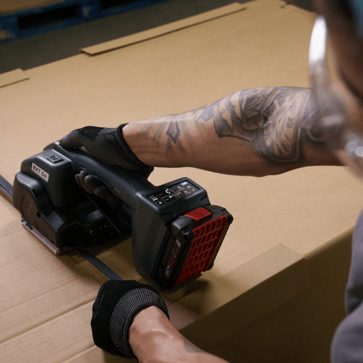 BXT Go Battery Powered Strapping Tool Securing a Carton | Maxpack Worker using a BXT Go battery powered strapping tool to secure a cardboard carton with strapping.